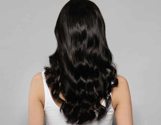 Rear View of A Woman with Long, Wavy Dark Hair Against a Gray Background — Hair Salon in Darwin, NT